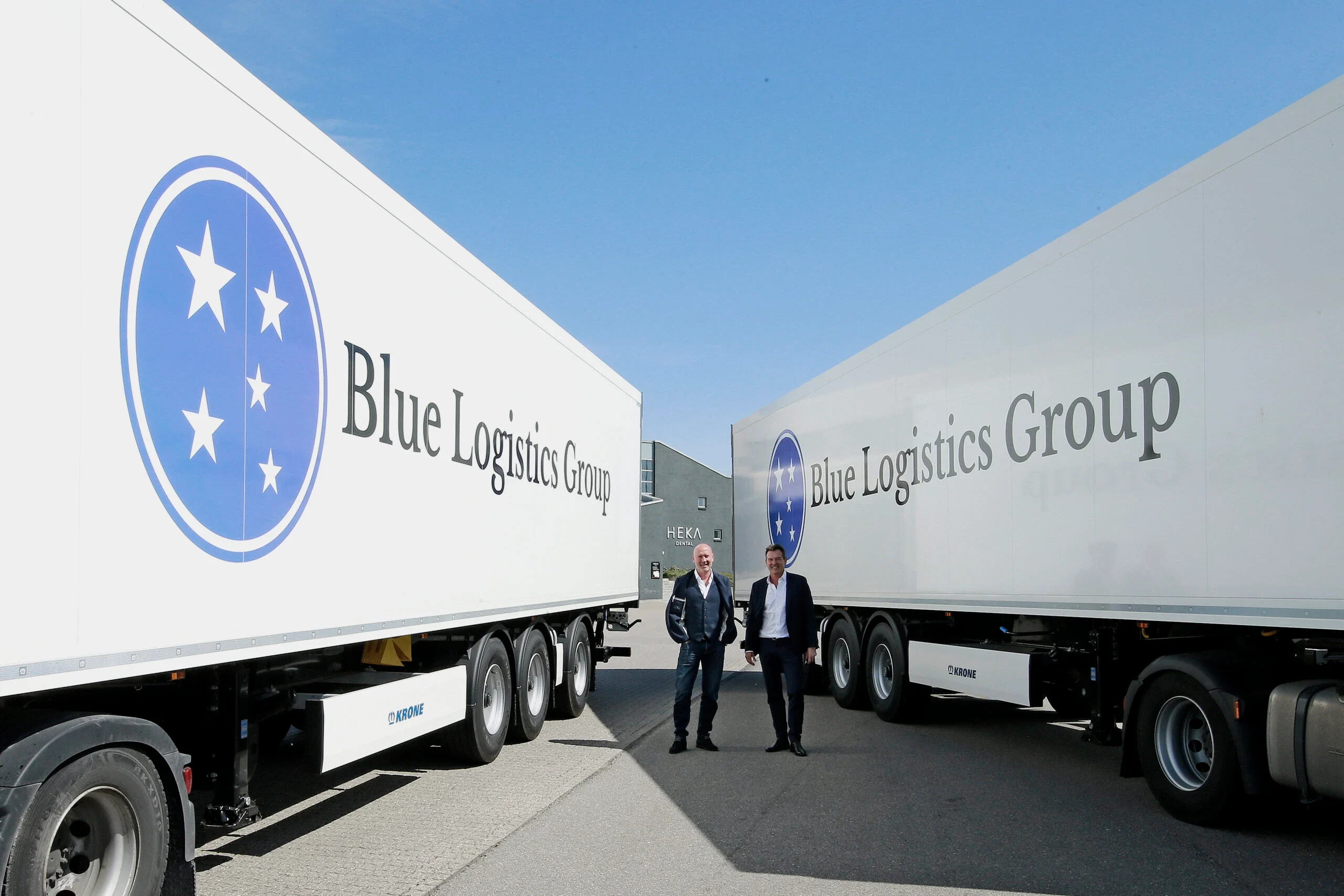 Blue Logistics Groups logotyp på en trailer, med två medarbetare framför